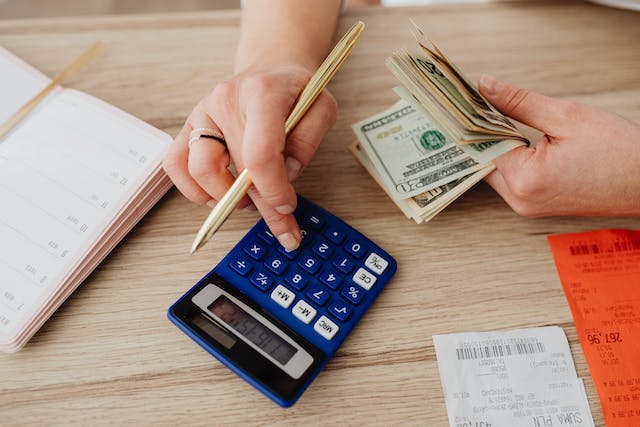 A person holding money and using a calculator.